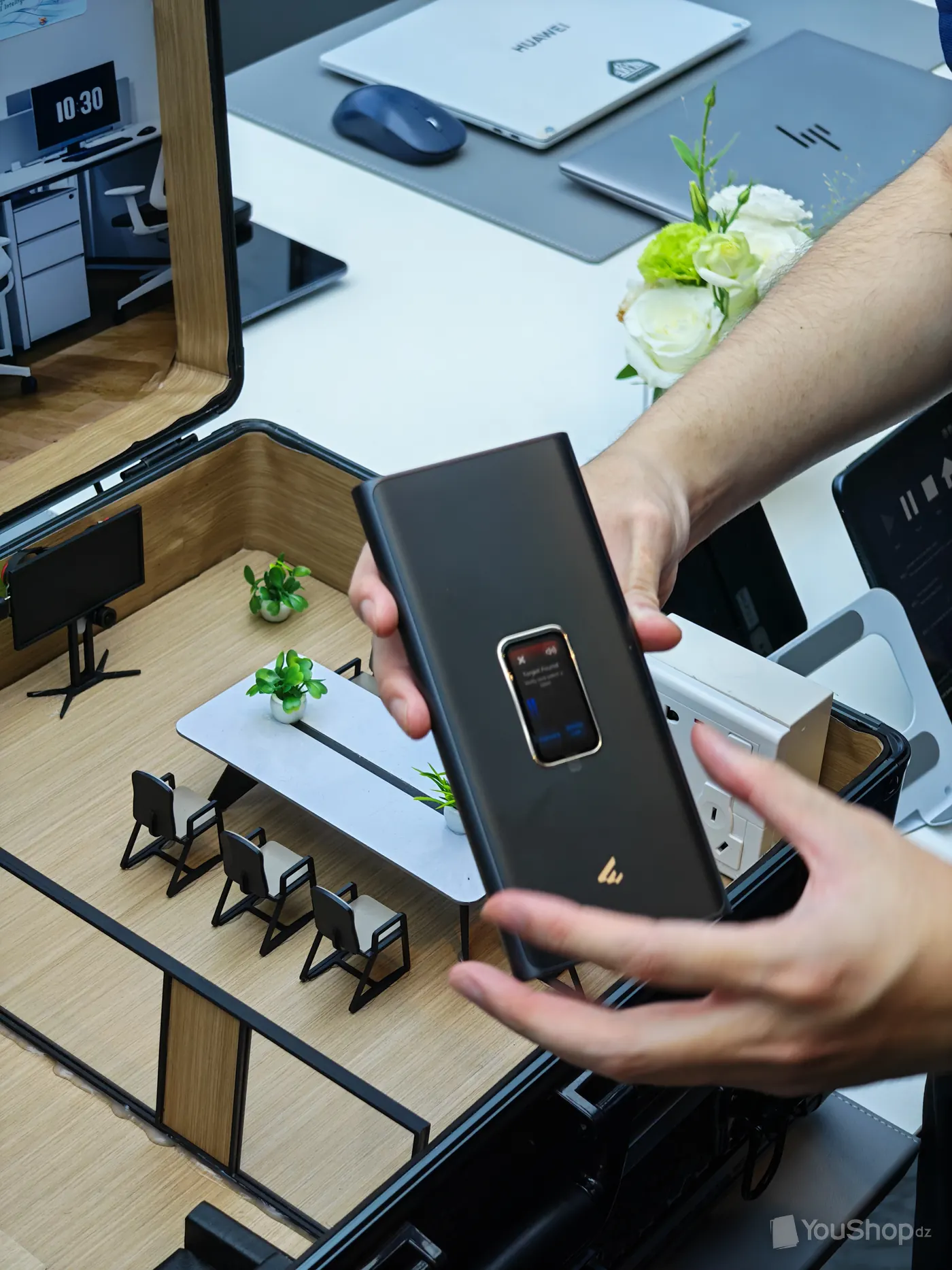 Appareil Huawei tenu au-dessus d'une maquette de plateau de bureau, petit écran allumé