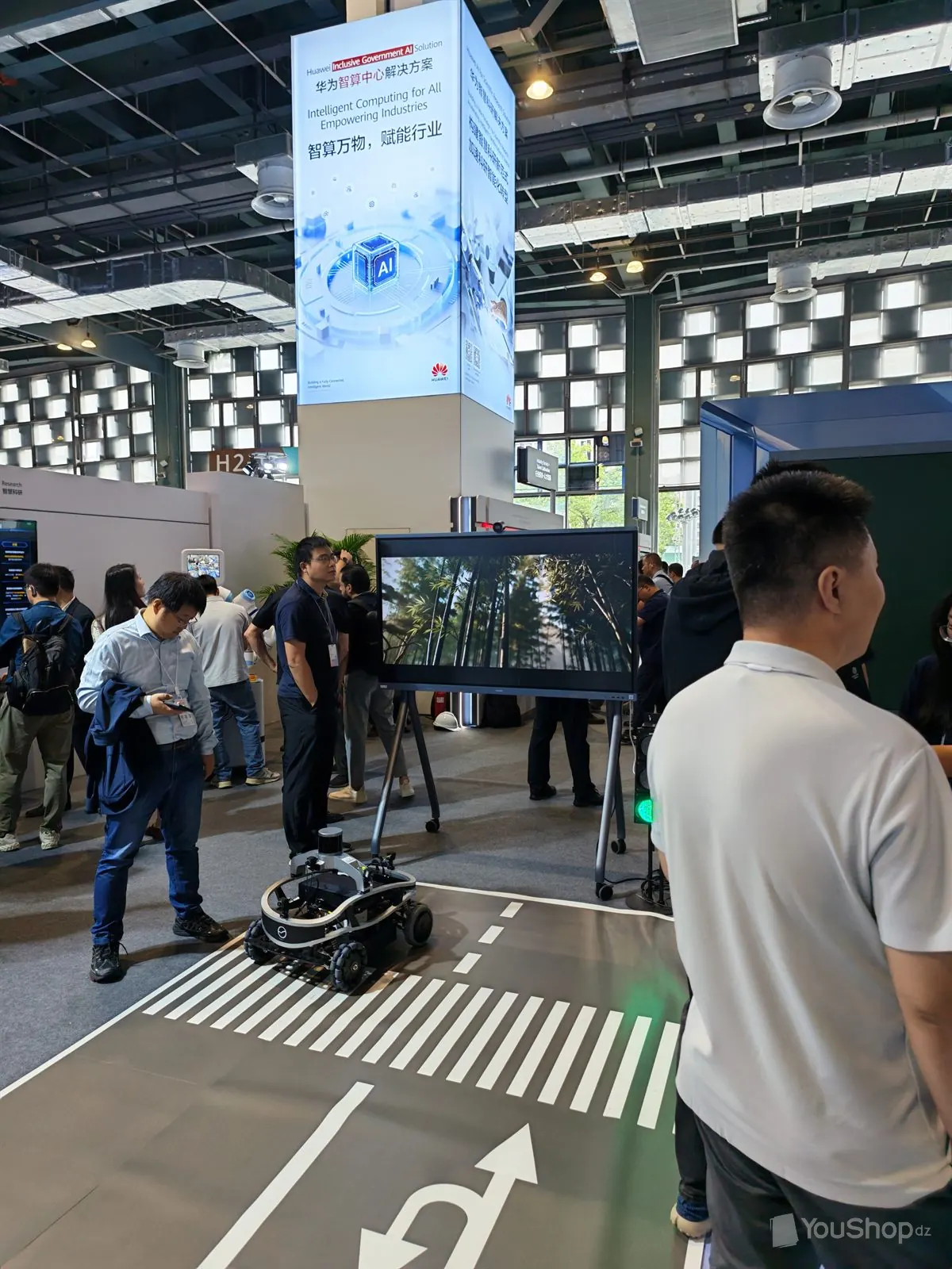 Petit véhicule autonome sur une route miniature peinte au sol devant une colonne Huawei